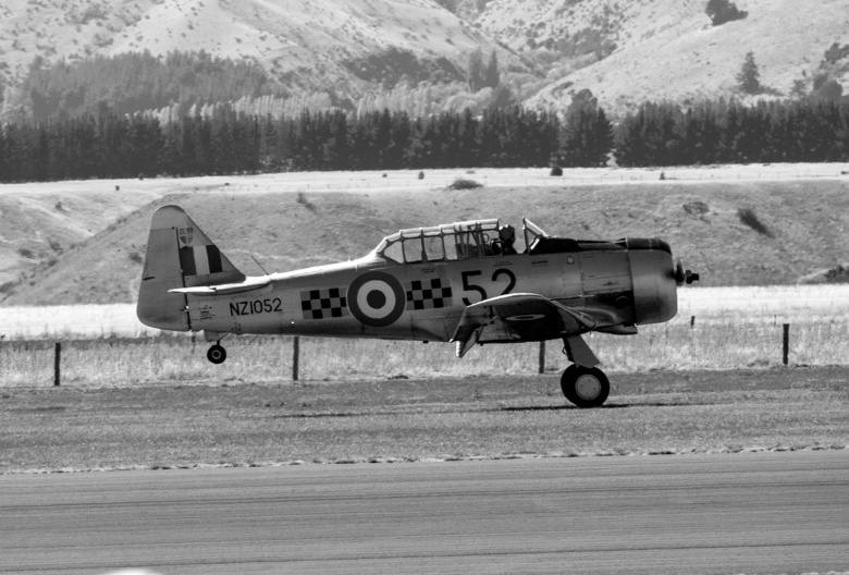 Photograph of a warbird aircraft landing onto a runway. Image is formatted in black and white, original by Katelyn Greer.